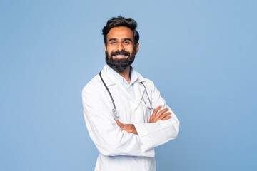 A confident Indian doctor is smiling warmly, dressed in a white lab coat with a stethoscope draped...