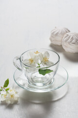 Fragrant jasmine tea in a glass cup with marshmallows on a white wooden table.