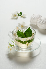 Fragrant jasmine tea in a glass cup with marshmallows on a white wooden table.