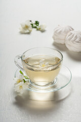 Fragrant jasmine tea in a glass cup with marshmallows on a white wooden table.