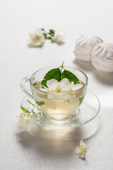 Fragrant jasmine tea in a glass cup with marshmallows on a white wooden table.