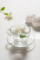 Fragrant jasmine tea in a glass cup with marshmallows on a white wooden table.