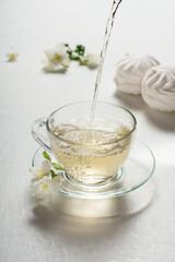 Fragrant jasmine tea in a glass cup with marshmallows on a white wooden table.