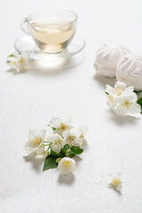 Fragrant jasmine tea in a glass cup with marshmallows on a white wooden table.