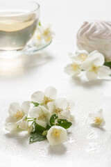 Fragrant jasmine tea in a glass cup with marshmallows on a white wooden table.