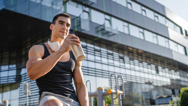 One caucasian man young male athlete take a brake during outdoor training in the park outdoor gym hold supplement shaker in hand happy confident strong copy space