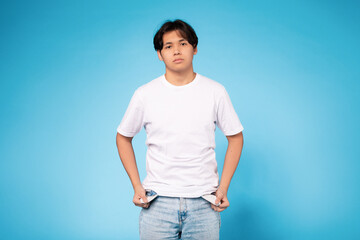 Asian young guy stands against a blue background, wearing a white shirt and jeans. He appears to be...