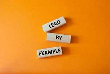 Lead by Example symbol. Concept word Lead by Example on wooden cubes. Beautiful orange background....