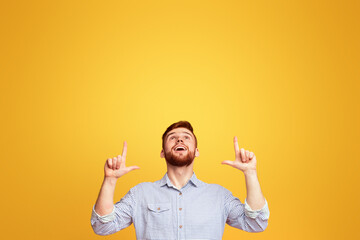 A man standing with hands in the air in front of a bright yellow background, pointing at copy space...