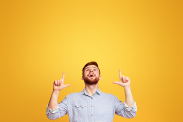 A man standing with hands in the air in front of a bright yellow background, pointing at copy space above him