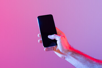 A person holds a smartphone with a dark, unlit screen against a gradient purple background. The...