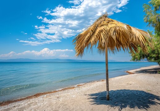 Summer beach: Paralia, Olympic Riviera, Pieria, Greece. Palm parasol shades the sand.
