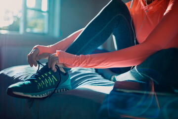 Woman tying running shoes at home before workout