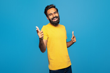 Indian man wearing a yellow t-shirt is enthusiastically giving a thumbs up gesture, showing...