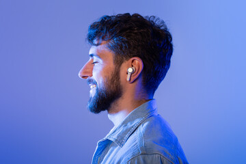 A bearded man is seen wearing ear buds, listening to music or audio content. He appears engaged and...