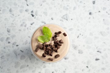 A top down view of a foamy coffee drink with chocolate shavings and mint leaf garnish.