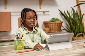 Multicultural female child sitting at table working on her homework assignment using her tablet