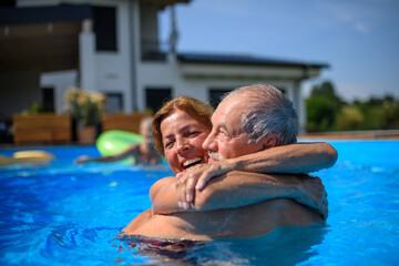 Couple of cheerful seniors shaving fun in pool with friends jumping, swiming and lounging on...