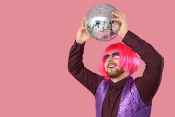 Handsome young man in wig with disco ball on pink background