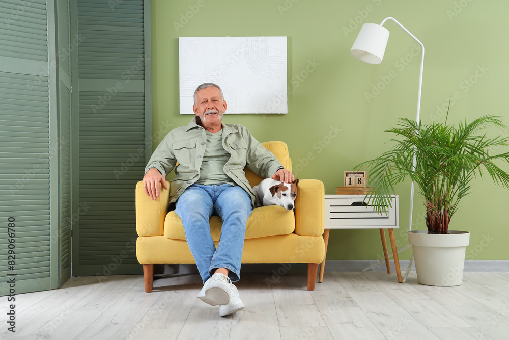 Wall mural Mature man with cute Jack Russell terrier sitting in armchair at home