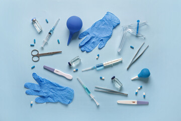 Gynecological speculum with pregnancy tests, medical gloves and pills on blue background