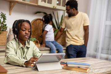 Obraz premium Little girl sitting at table working on her homework assignment using her tablet at home