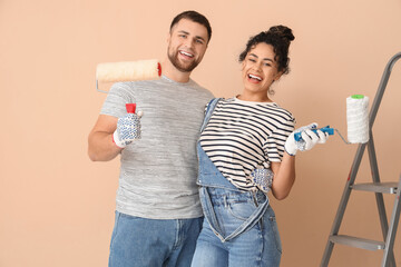 Beautiful young happy couple with paint rollers near beige wall doing repair in new house