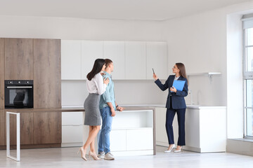 Female real estate agent with clipboard showing young couple kitchen in new house