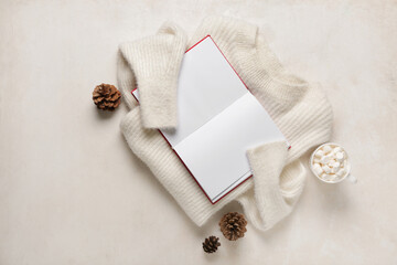 Cup of hot cocoa with book and jumper on white background