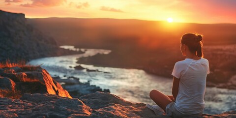 Obraz premium A tranquil scene with a person sitting at the edge of a canyon, watching a beautiful sunset over a winding river