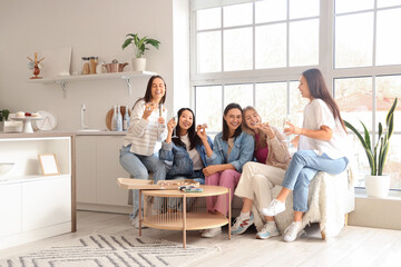 Young women with champagne eating tasty pizza at hen party in kitchen