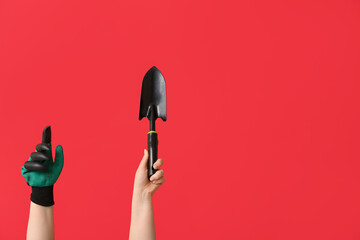 Female hands with gardening shovel and glove on red background