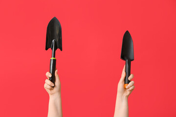 Female hands with gardening shovels on red background