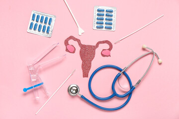Paper uterus with pills, gynecological speculum and stethoscope on pink background