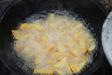 Potatoes are fried in a large pan in a cauldron, close-up view from above. Cooking in nature