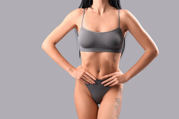 Beautiful young woman in grey underwear on light background