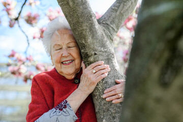 Portrait of elderly woman standing by magnolia tree, in park, having relaxing moment. Grandmother...