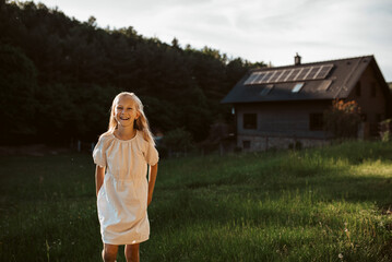 Young girl in front of house with solar panels on roof. Concept of renewable resources.