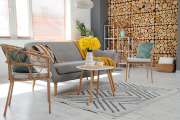 Grey sofa, armchairs, coffee table and vase of narcissus flowers in beautiful living room