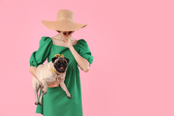 Surprised young woman with cute pug dog on pink background