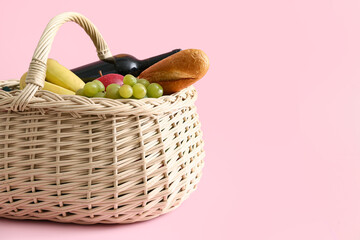 Wicker basket with tasty food and drink for picnic on pink background
