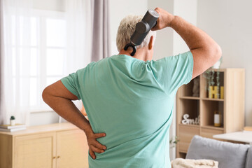 Mature man massaging his neck with percussive massager at home, back view