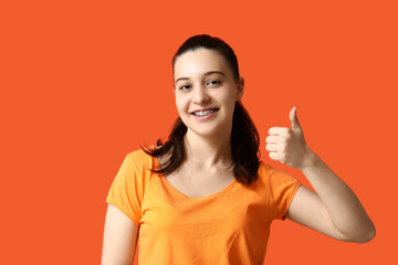 Young woman in stylish orange t-shirt showing thumb-up on color background