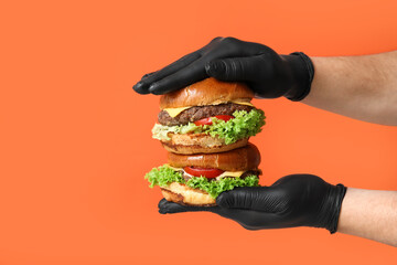 Male hands in black gloves holding tasty burgers on orange background