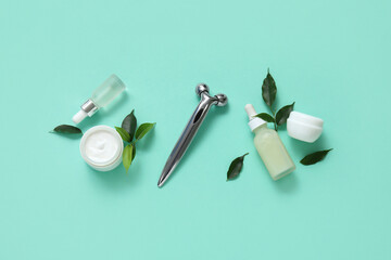 Facial roller with serum, cosmetic cream and green leaves on turquoise background