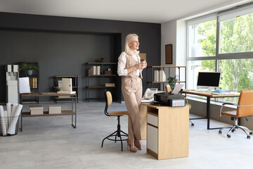 Mature businesswoman with cup of coffee and printer in office