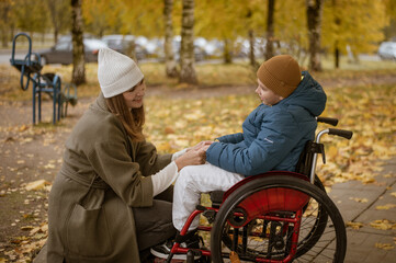 a 10-year-old boy in a wheelchair walks in the fall with his mother on the street with a dog on the playground. High quality photo
