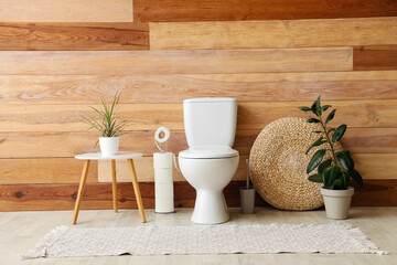 Interior of restroom with toilet bowl, coffee table and houseplant near wooden wall