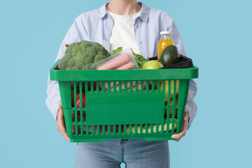Young woman with full shopping basket on blue background, closeup