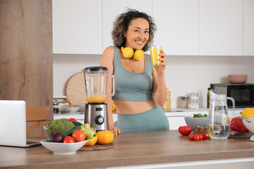 Sporty mature woman with healthy smoothie and blender in kitchen